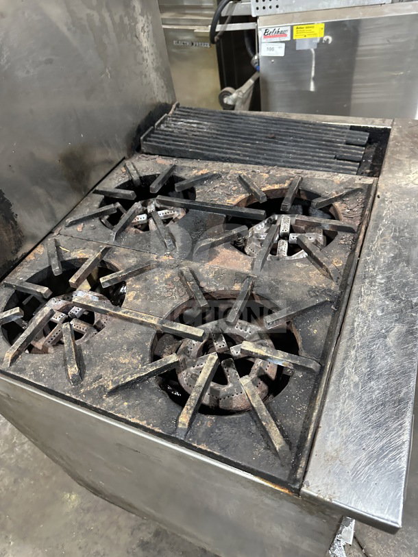 Commercial stainless steel gas range with 4 open burners, 12" charbroiler, standard oven, and wired rack. On legs.