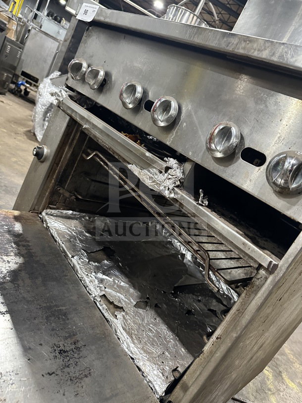 Commercial stainless steel gas range with 4 burners, 12" charbroiler, standard oven, wired rack, and legs, some wear visible.