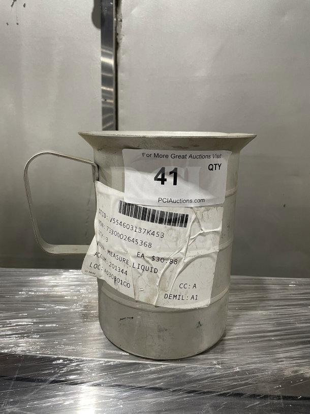Brand new stainless steel liquid measuring cup, commercial surplus, with handle and visible auction and item tags.