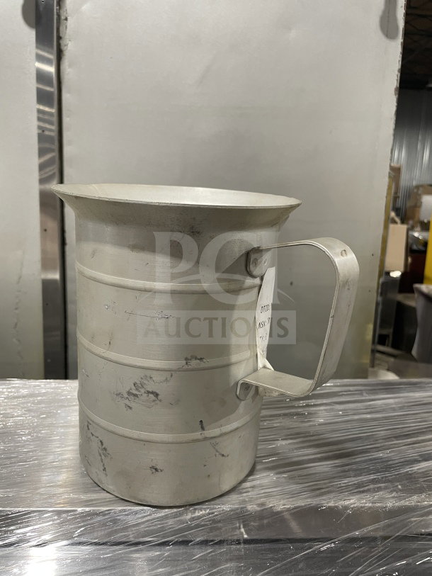 Brand new commercial stainless steel liquid measuring cup, sturdy handle, shows minor surface marks, large capacity.