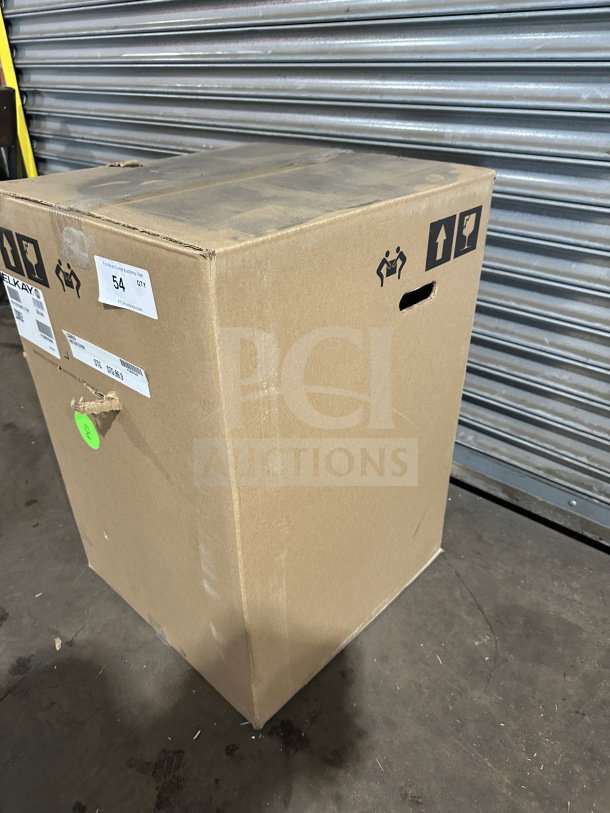 Cardboard box containing a new Elkay LZS8WSLP hydration station with labels indicating model and handling instructions. Box on concrete floor.