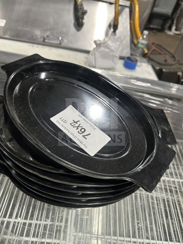 Commercial oval black Bakelite thermal underliner with handles, in stack. Label indicates "7X Your Bid". Durable and sleek.