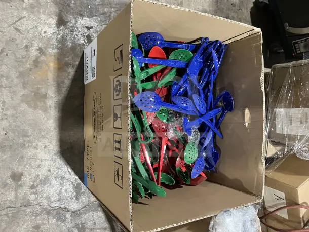 Assorted poly serving spoons and tongs in red, green, and blue, packed in a large box. New condition.