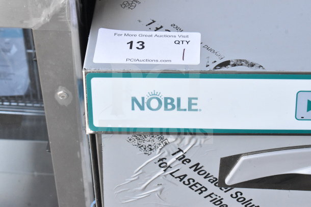 Brand new Noble 495LTUC24 undercounter dishwasher, low-temp, 120V, visible logo, minor scratches, auction tag attached.