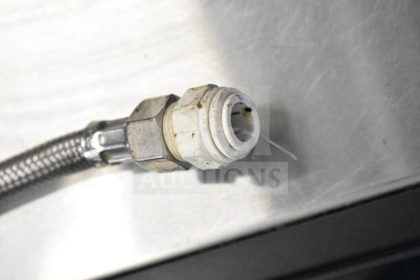 Braided metal hose with a plastic fitting, partially stained, connected to a Schaerer Barista espresso machine.