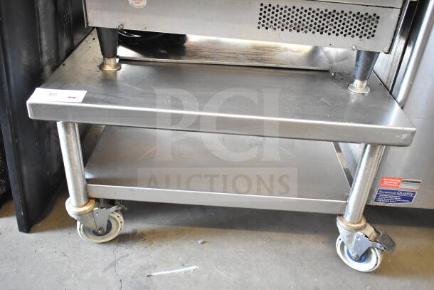 Commercial equipment stand with under shelf on casters, stainless steel, sturdy, used condition, visible quality assurance label.