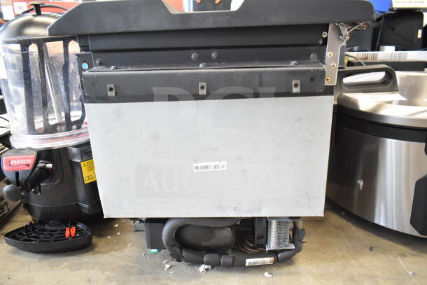 Mini cooler with black and metallic exterior, visible cooling components, and a label indicating lift points; wear on surface.