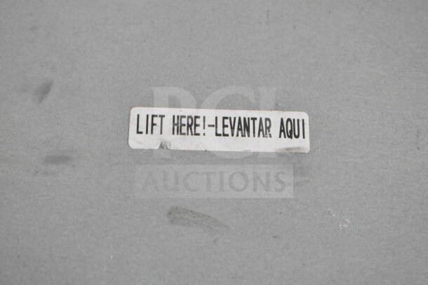Label on mini cooler reading "Lift Here! - Levantar Aquí" on cardboard surface.