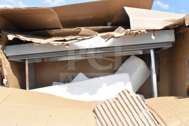 Cardboard box containing 18 brand new, scratch and dent items, including a taco holder, fry pan, and trash can.