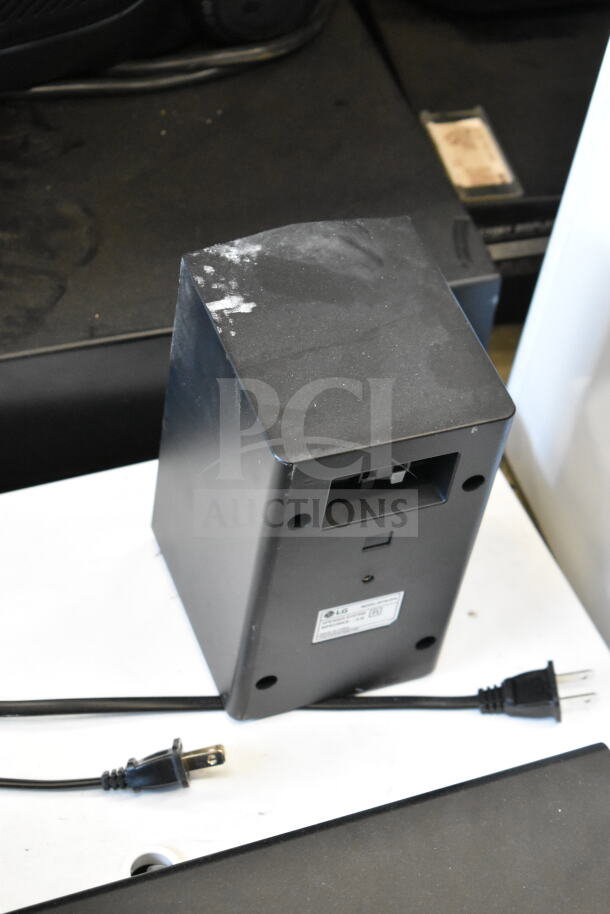 Store display with LG sound bar, four speakers, visible power cord. Minor wear and label indicating model details.