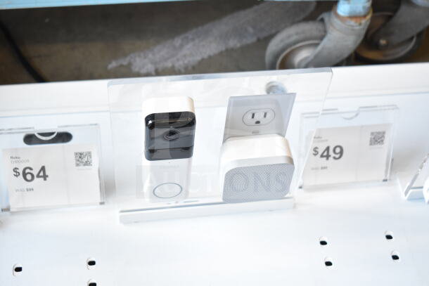 Store display featuring Roku camera model DB1000R priced at $64. Includes additional accessories and pricing tags.