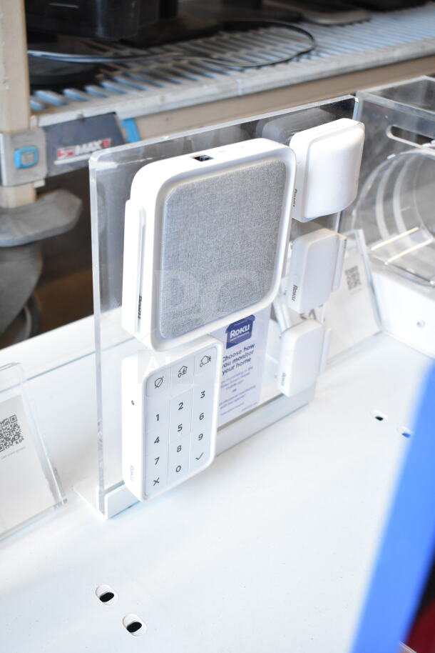 Store display featuring Roku camera and smart home products, including keypad and sensors, in excellent condition.