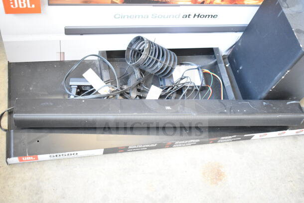 Store display with JBL SB580 sound bar and speaker, visible wiring, and branded packaging. Condition shows some dust.