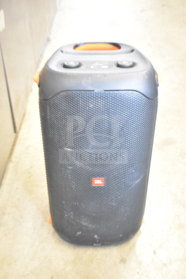 JBL speaker with black grille and orange accents, sturdy handle, lightly used condition, model visible on display.