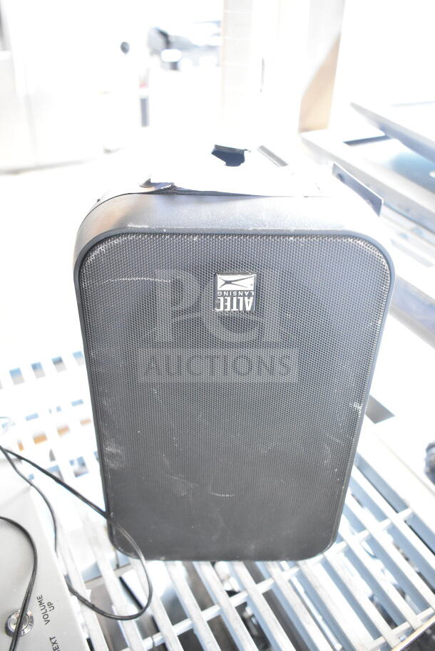 Altec Lansing speaker with black grille, visible surface wear, and brand logo; features open input ports and attached cables.