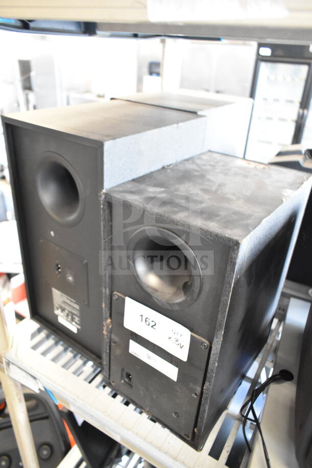 Three speakers including Samsung PS-WR45BB and Anatel Cinema SB580, showing used condition with visible labels and tags.