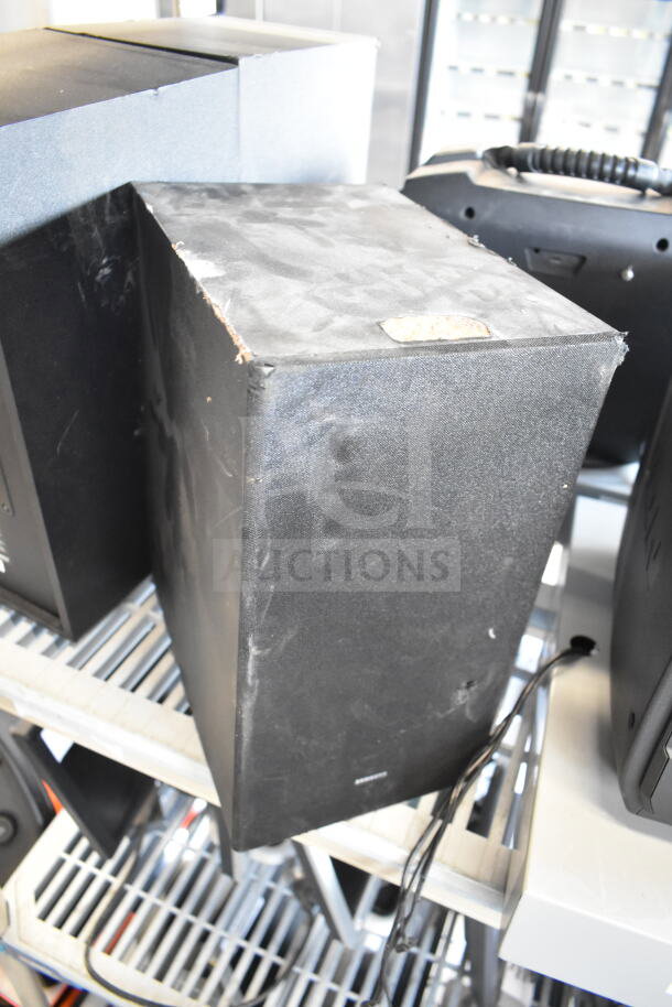 Three speakers, including Samsung PS-WR45BB and Anatel Cinema SB580, showing wear and placed on a metal shelf.