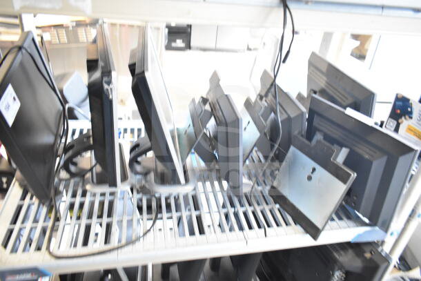Seven assorted monitors, including Dell, on a shelf. Mixed models and conditions, some with visible cords and mounting brackets.