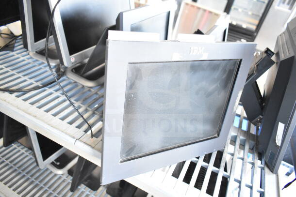 Seven mixed monitors including Dell and IBM models, used condition. Various sizes, showing screens and stands on a shelf.