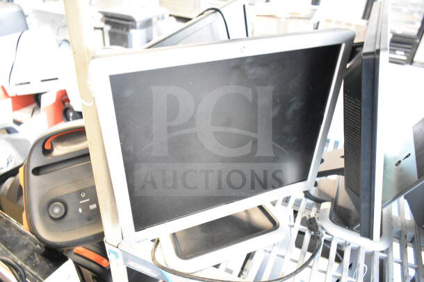 Seven assorted monitors, including Dell, stacked on a metal rack. Screens are visibly dusty. Auction lot offers seven times the bid.