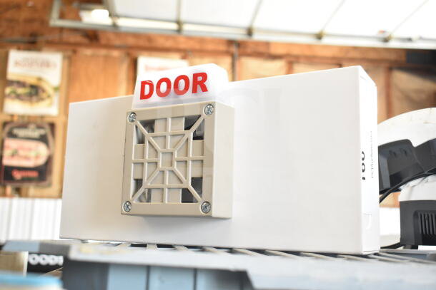 White emergency sign with "DOOR" label in red, featuring a front grill. Mounted fixture, in good condition.