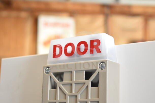 White emergency sign with "DOOR" in red text, mounted on a beige fixture with visible screws, indicating directional use.