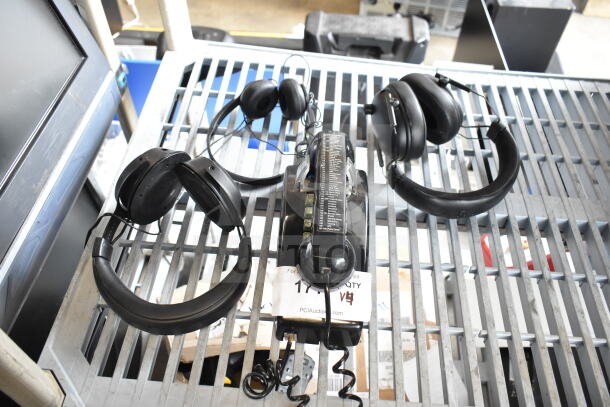 Four items including three headphones and a telephone on a gray metal rack. Mix of over-ear and on-ear designs.