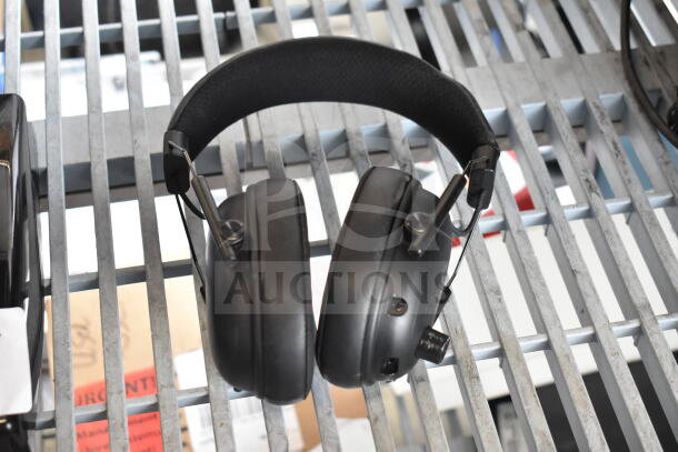 Headphones with adjustable band and padded ear cups, in fair condition, resting on a metal surface.