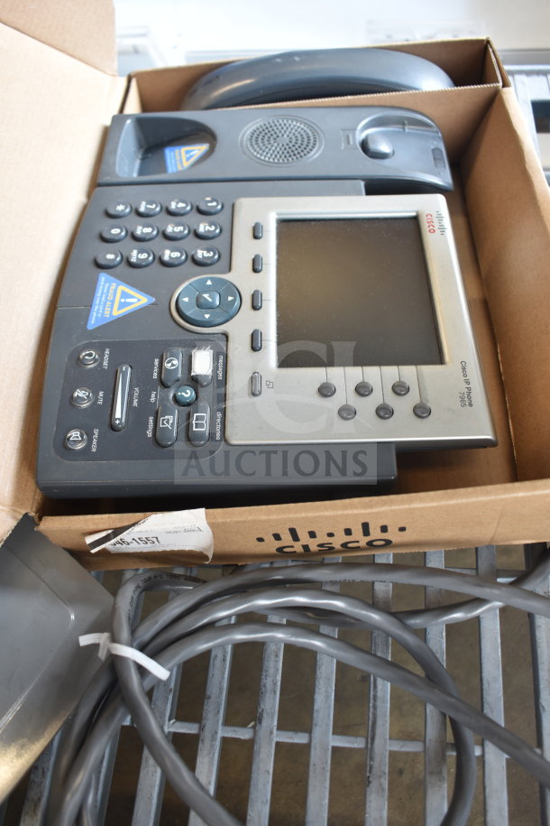 Cisco IP Phone 7965 in box with visible buttons and screen, alongside a Sensormatic ZBSMPCPEF security tag. Includes cables.