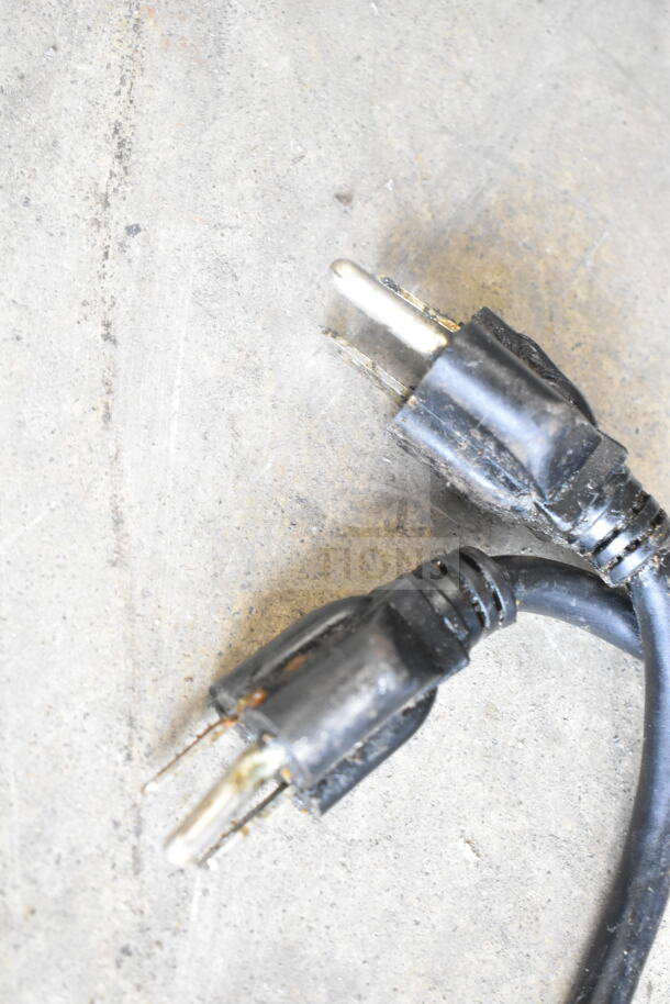 Black electrical plug with visible wear on a concrete surface.