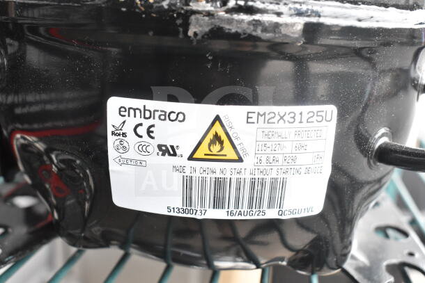 Brand new scratch and dent Embraco EM2X3125U compressor, 115-127V, 1 phase. Labels indicate CE compliance and fire risk.