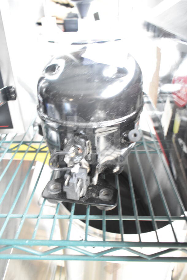 BRAND NEW Cubigel NUT70NR Avantco compressor, 115-127V, 1 phase, with scratch and dent, on metal rack shelf.