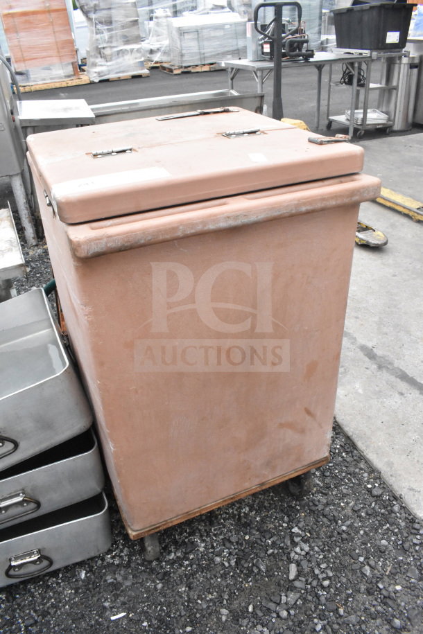 Food carrying case on dolly, tan color, rectangular shape, latches on lid, worn condition, on wheels for easy transport.