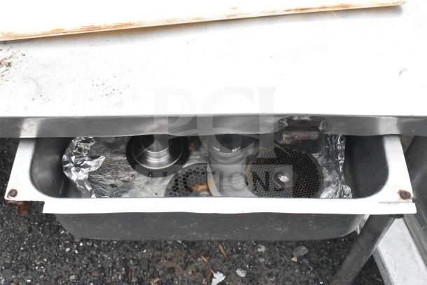 Commercial metal table with integrated drawer, showing signs of wear. Drawer contains metal components and foil.