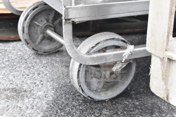 Metal cart with three tiers on commercial casters, highlighting wear and sturdy construction on rough surface.