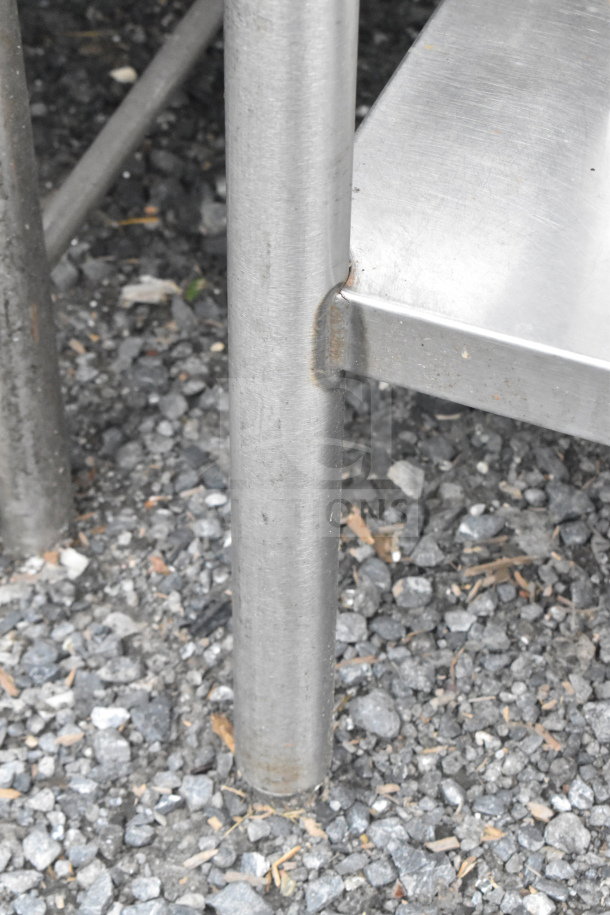 Stainless steel leg of a commercial table on gravel surface, part of auction lot including coolers, dunnage rack, rice cooker.
