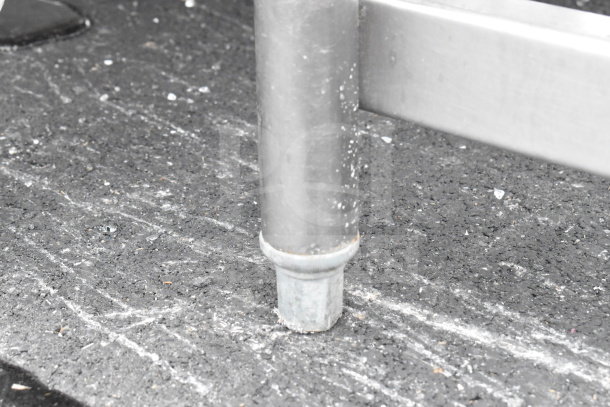 Close-up of a commercial table leg on asphalt. Silver metal with visible wear, indicating used condition.