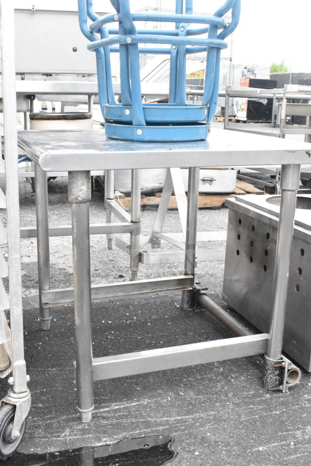 Stainless steel commercial table and two blue metal stools, slightly used, visible outdoor setting.