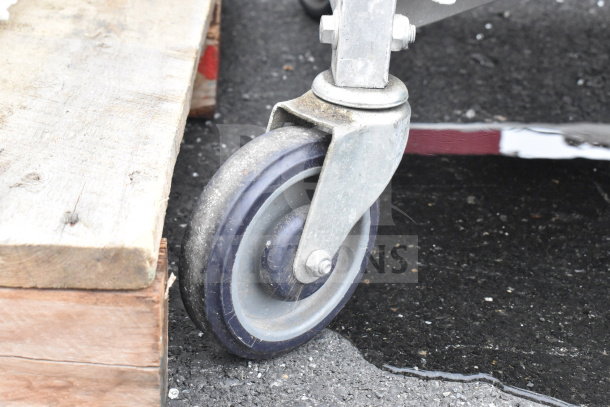 Close-up of a commercial caster wheel attached to a transport pan rack, showing sturdy metal construction and well-used condition.