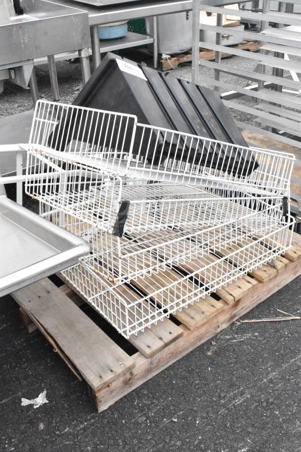 Metal storage baskets, white, stacked on a wooden pallet. Includes black bins with visible wear. Ideal for bulk storage.