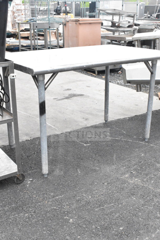 Stainless steel commercial table with sturdy metal legs, used condition, scratch marks visible on surface, industrial setting.