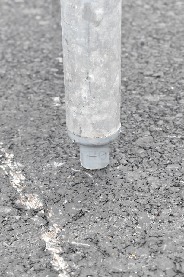A metal leg of a commercial table on an asphalt surface, showing rust and wear, indicating use.