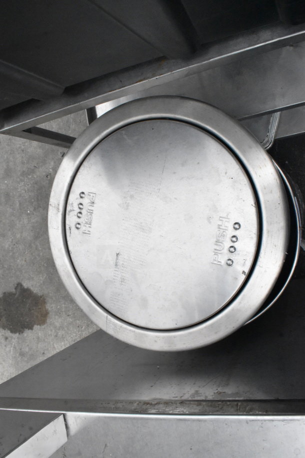 Stainless steel Simplyhuman trash can with push lid, showing signs of use, marked "PUSH" on top surface.