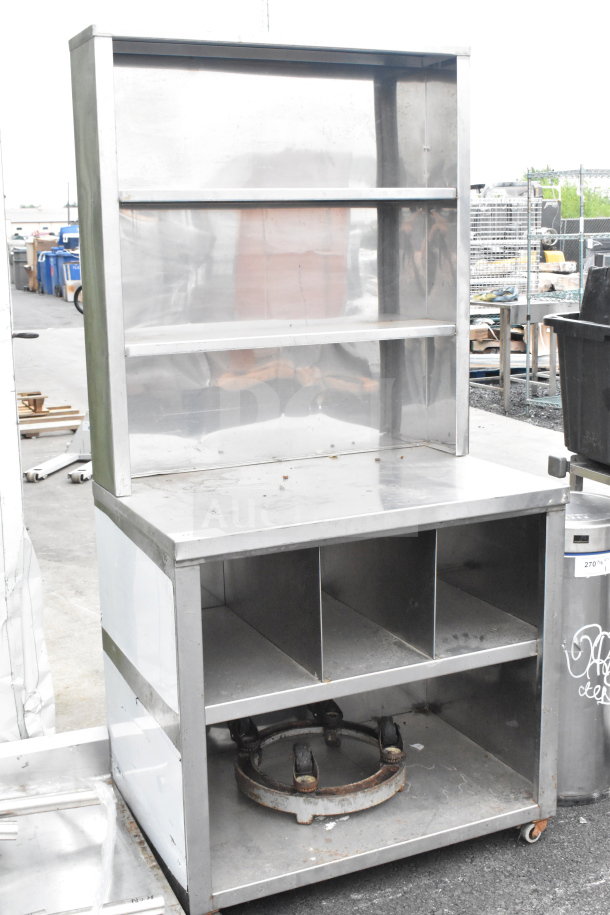 Commercial counter with two over shelves and two under shelves on casters, made of stainless steel, shows signs of use.