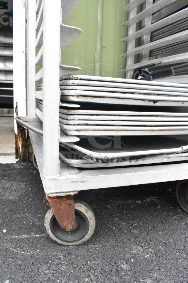 Commercial pan transport rack with 10 baking pans on casters, some rust on wheels; suitable for bakery use.