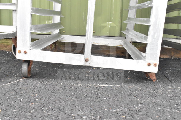 Commercial pan transport rack with multiple slots and commercial casters, showing signs of rust and wear.