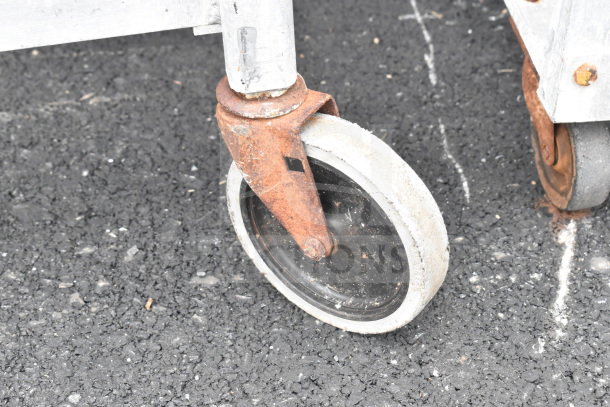 Commercial pan transport rack with industrial caster, showing rust on metal parts, indicating wear.