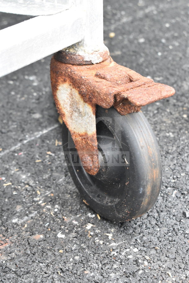 Rusty caster wheel of a commercial pan transport rack on asphalt, showing significant wear.
