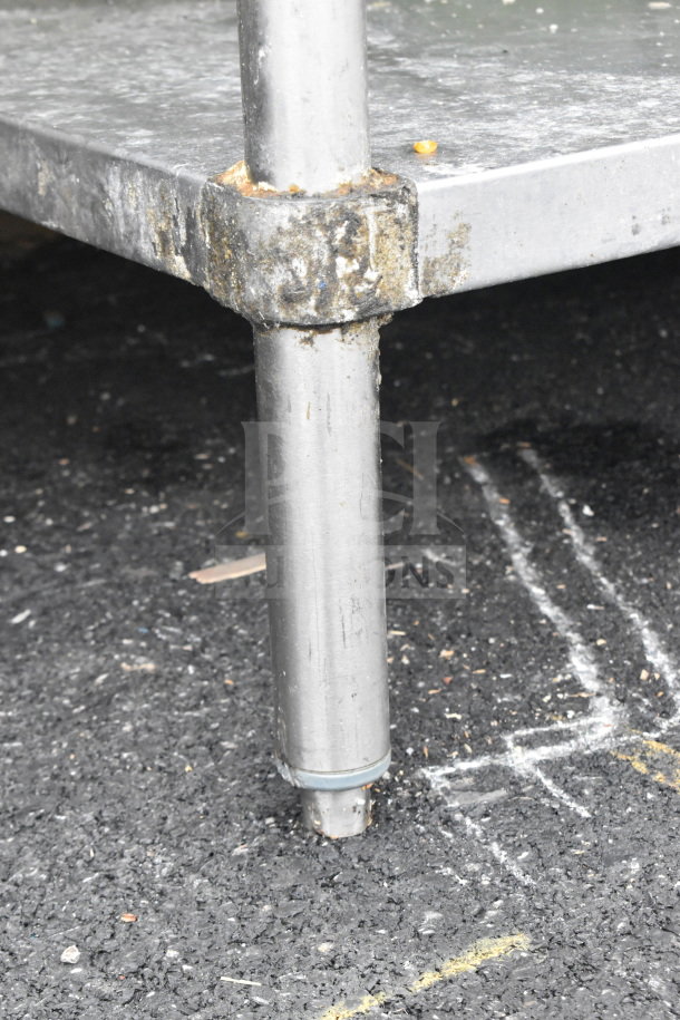 Industrial metal table leg with visible wear, supporting a commercial table with an under shelf, showcasing durability.