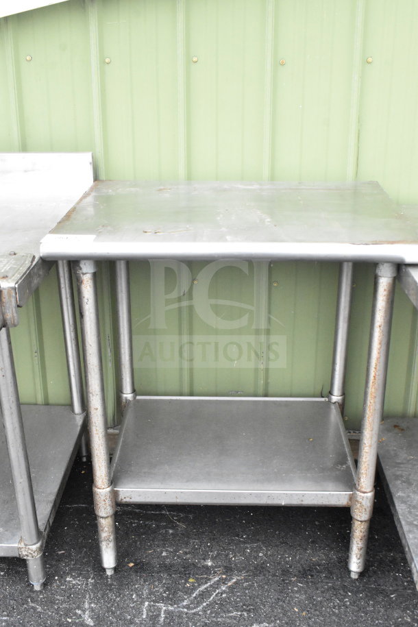 Commercial metal table with under shelf, noticeable wear and rust on legs, suitable for practical use.
